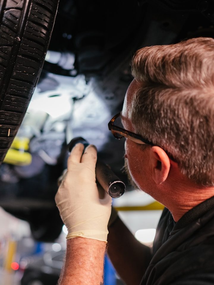 Mechaniker untersucht ein Auto mit einer Taschenlampe.