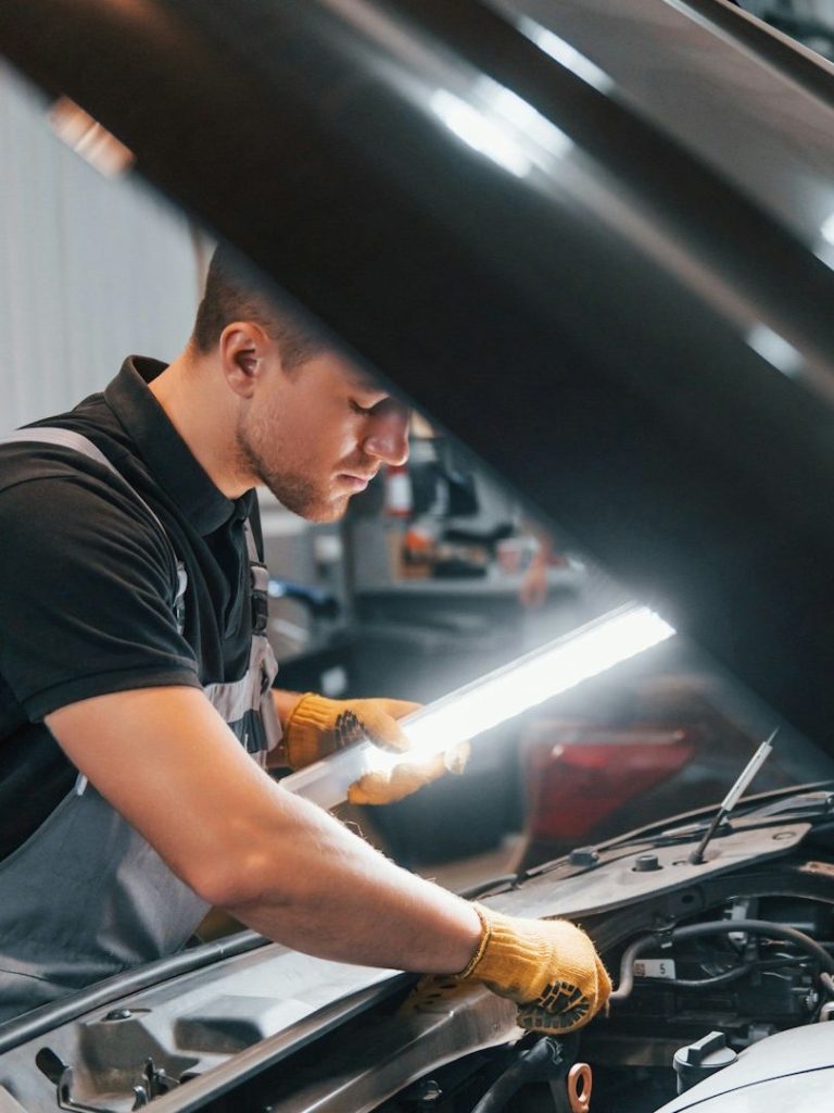 Ein Mechaniker arbeitet an einem Fahrzeugmotor mit einer Taschenlampe.