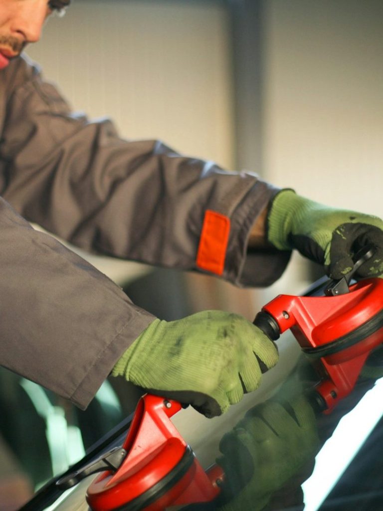 Ein Mann in Arbeitshandschuhen verwendet Saugnäpfe, um ein Auto-Glas zu heben.