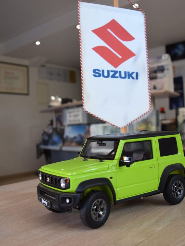 Modell eines grünen Suzuki Jimny vor einem Suzuki-Werbeschild.