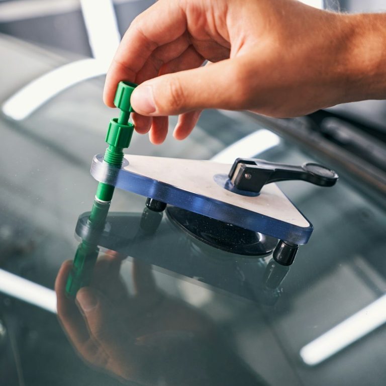 Hand, die das Reparaturwerkzeug auf einen Steinschlag bei einer Autoscheibe hält. 