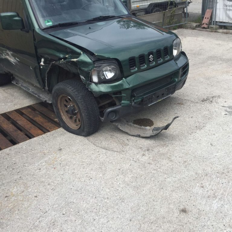 Grünes Auto mit beschädigtem vorderem Stoßfänger und kaputter Seite.