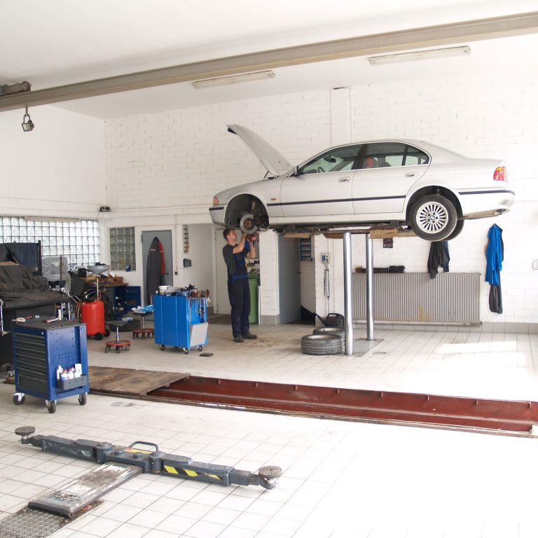 Mechaniker arbeitet an einem hochgehobenen Auto in einer Werkstatt.