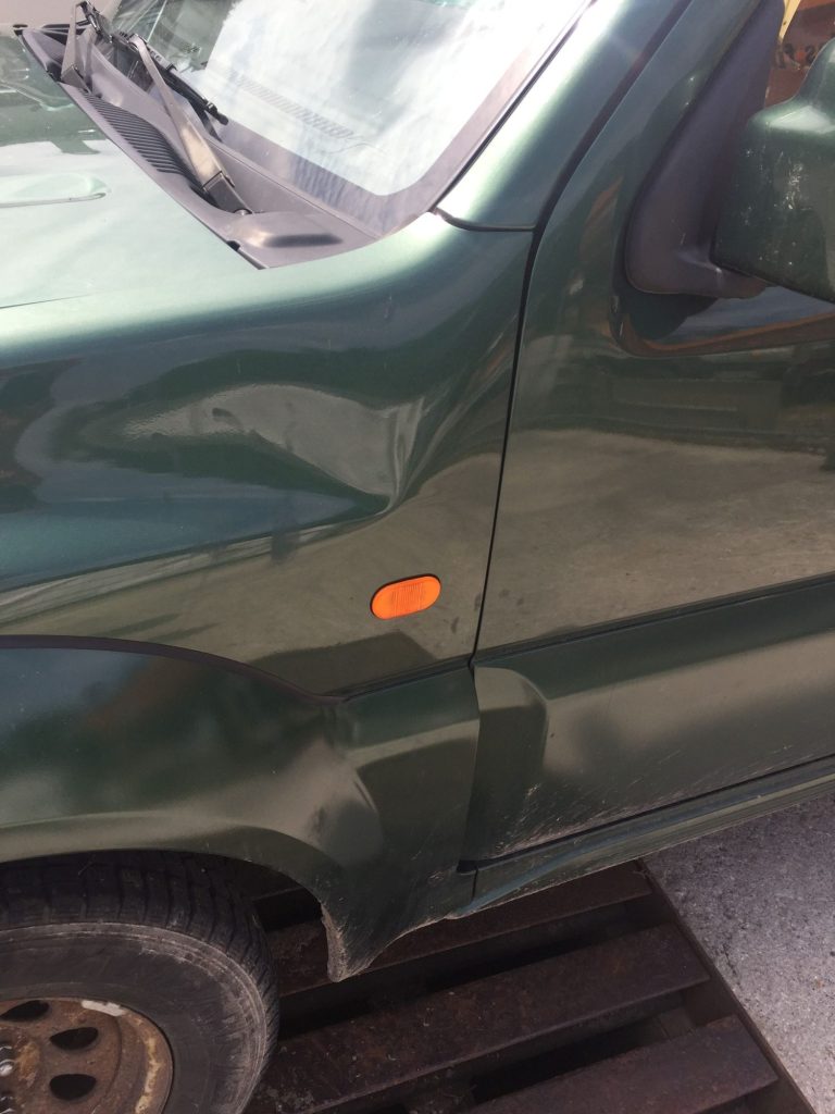 Grünes Auto mit einer Delle am linken Kotflügel.